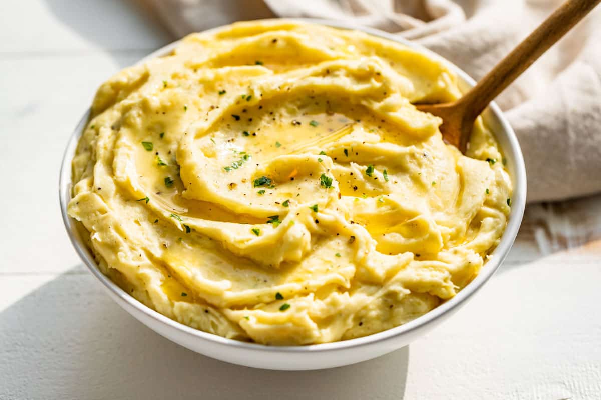 Side view of mashed potatoes in a white bowl topped with melted butter and chopped parsley.