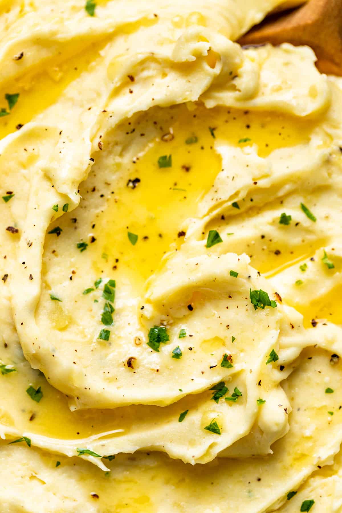 Close macro shot of mashed potatoes topped with melted butter and chopped parsley.