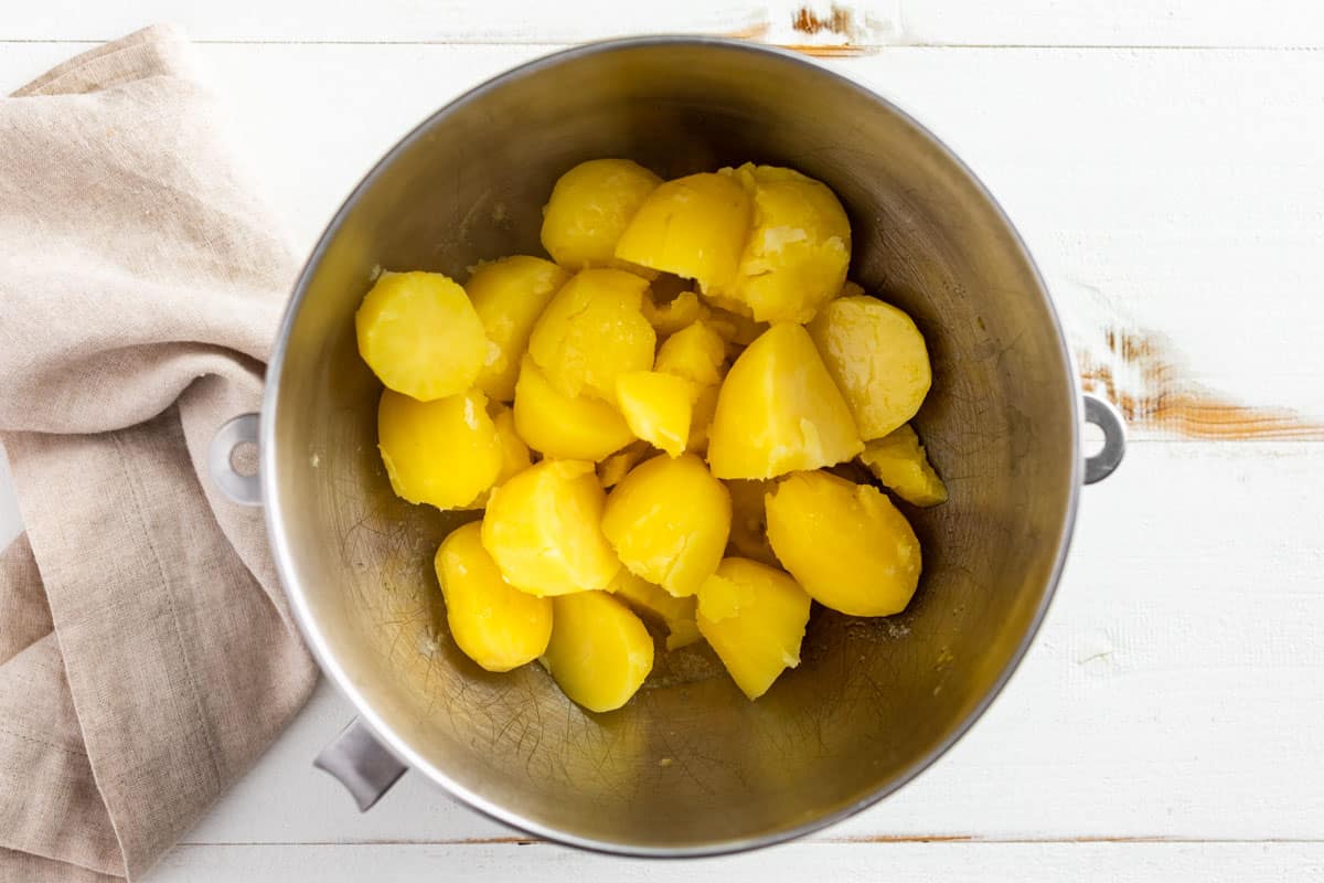 Cooked potatoes being added to a mixing bowl.