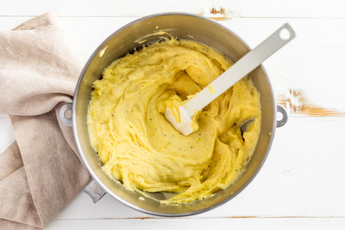 Adding the half and half to the mashed potatoes in a mixing bowl.
