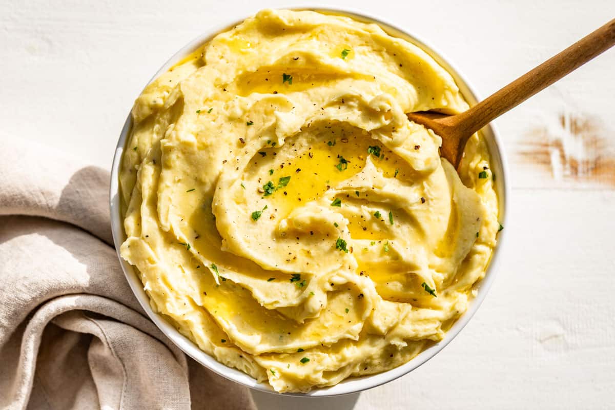 Straight down view of a white bowl of mashed potatoes topped with melted butter and chopped parsley.