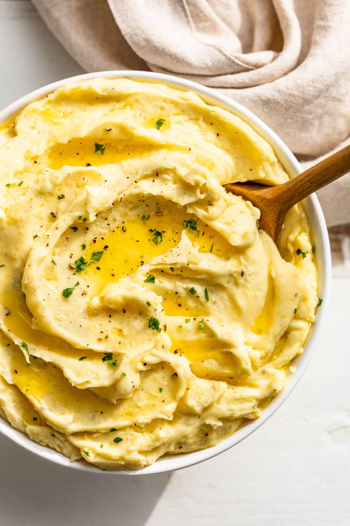 Straight down view of mashed potatoes in a white bowl with a wood spoon and sprinkled with parsley.