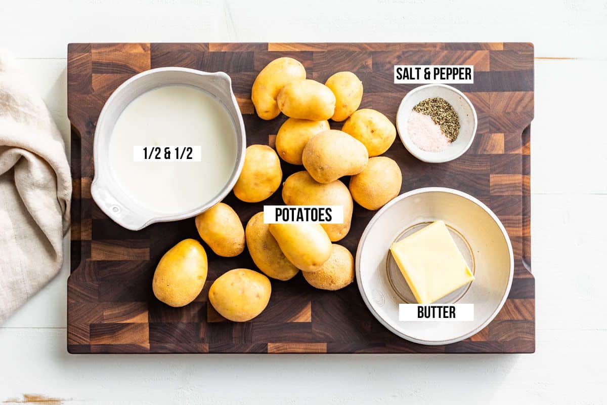 Potatoes, half and half, butter, sea salt and pepper in bowls on a wood cutting board.