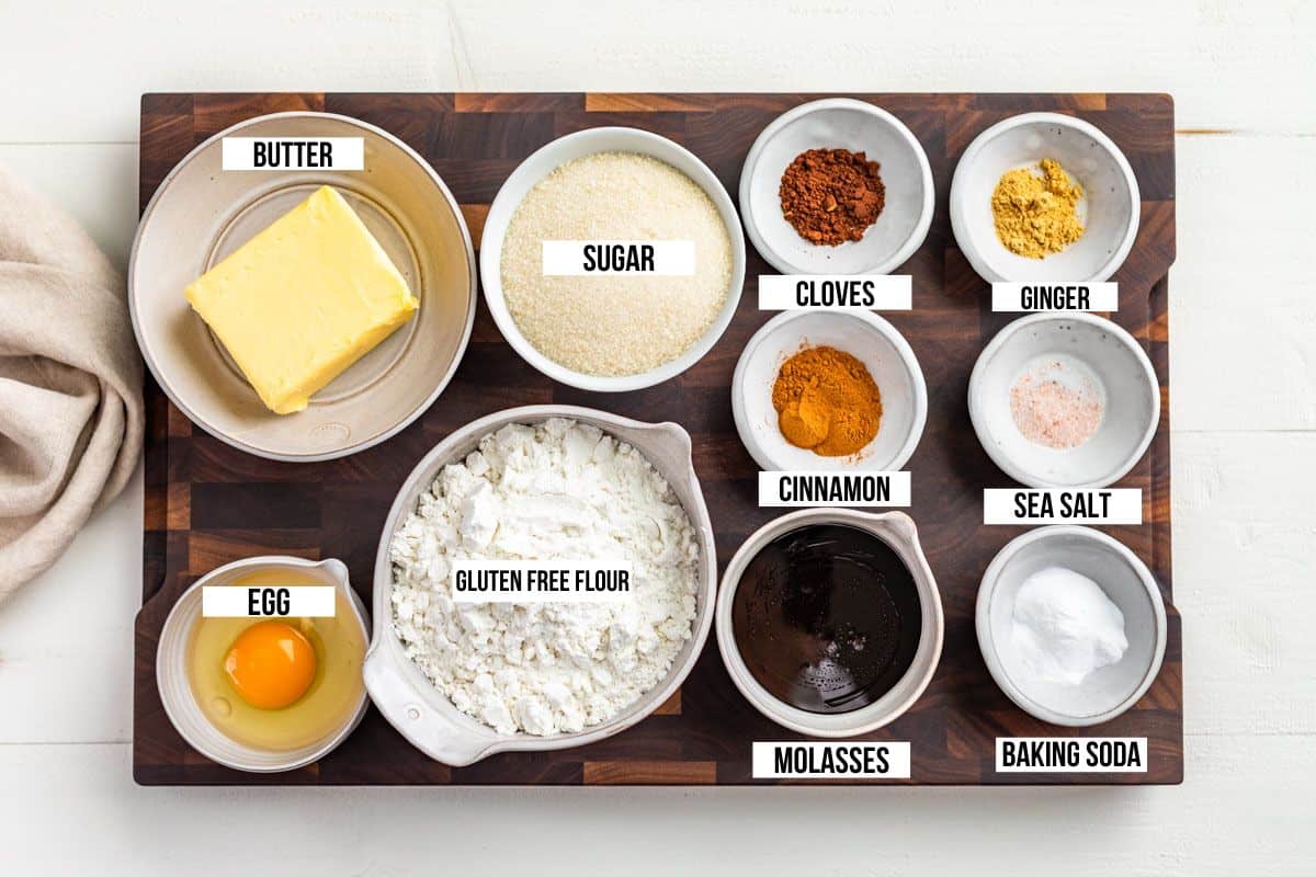 Butter, sugar, egg, molasses, ginger, cinnamon, ginger, salt, and flour in small container on a wood cutting board.