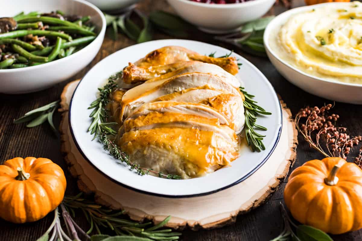 A platter of sliced turkey surrounded by green beans, mashed potatoes, and decorative pumpkins.