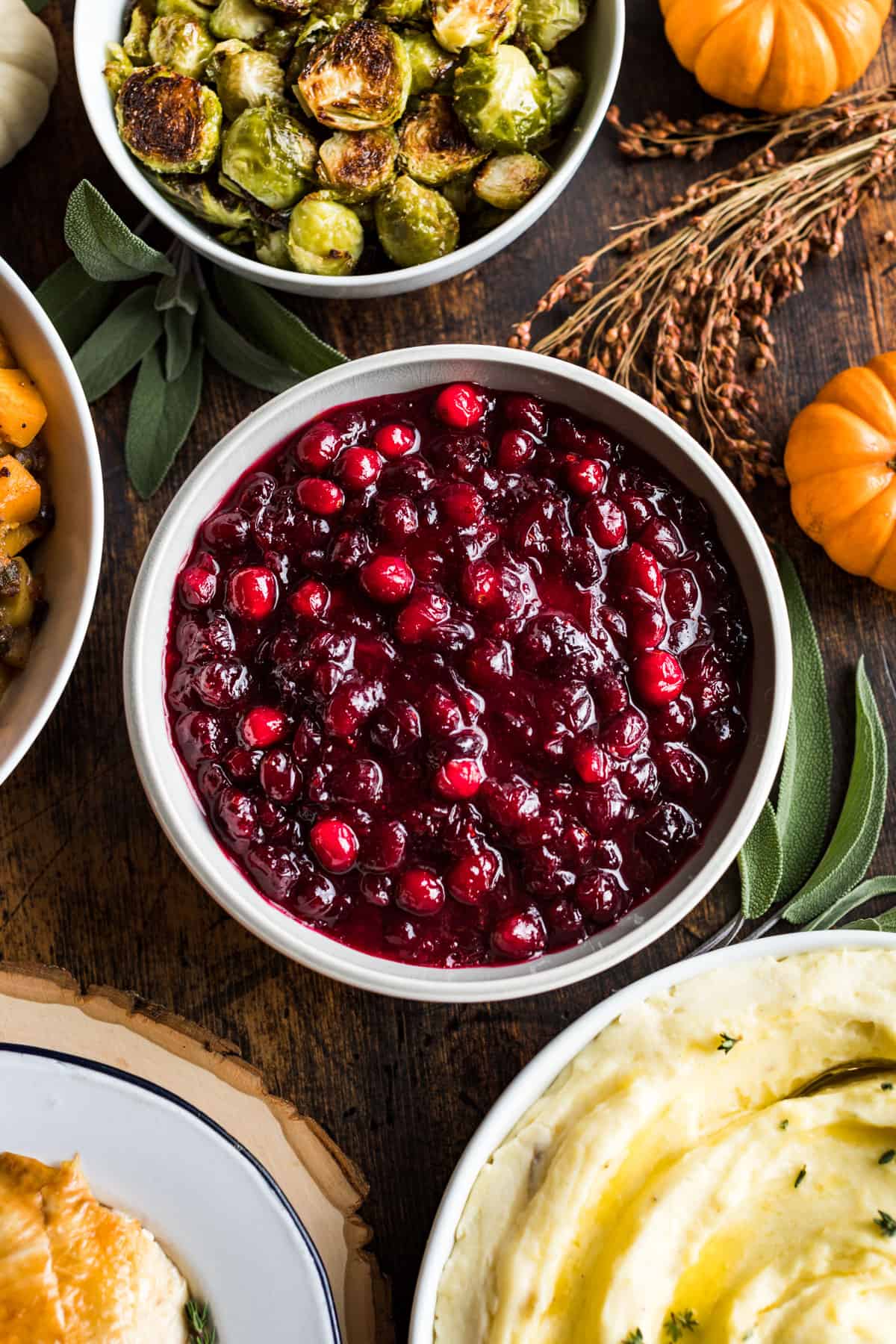 A bowl of cranberry sauce in the center surrounded by stuffing, turkey, mashed potatoes and brussels sprouts.
