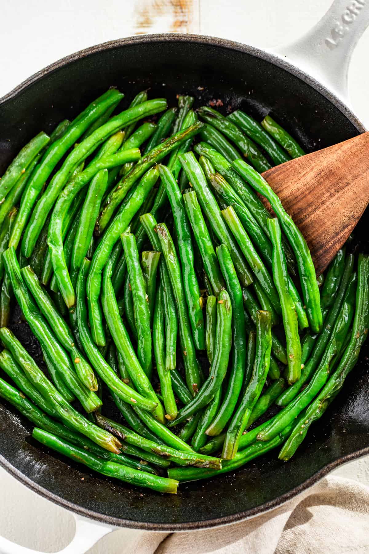 Closer downwards view of green beans in a white skillet.