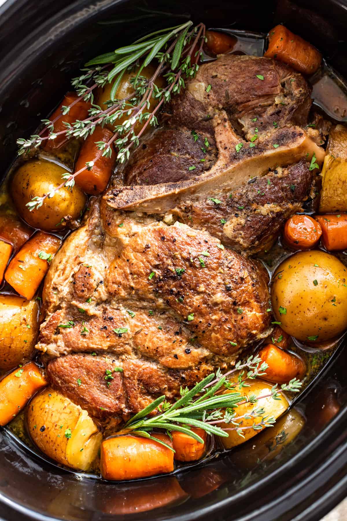 Close up view of the Slow Cooker Pork Roast in a slow cooker bowl turned at an angle with fresh herbs on top.