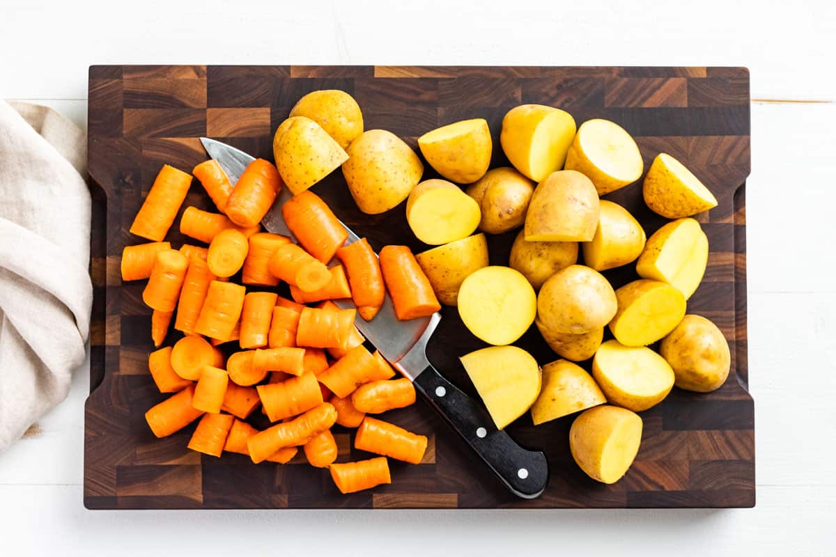 Cut up carrots and potatoes on a wood cutting board.
