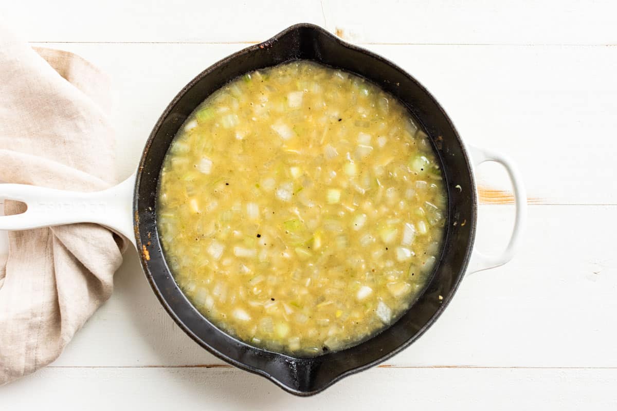 Adding the onions, garlic, and chicken broth to the cast iron pan after the roast has been seared.