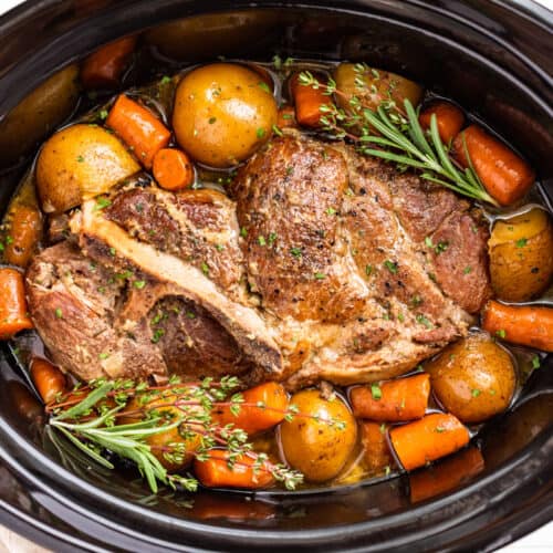Finished Slow Cooker Pork Roast surrounded with potatoes and carrots and topped with sprigs of thyme and rosemary.