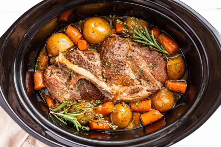 Finished Slow Cooker Pork Roast surrounded with potatoes and carrots and topped with sprigs of thyme and rosemary.