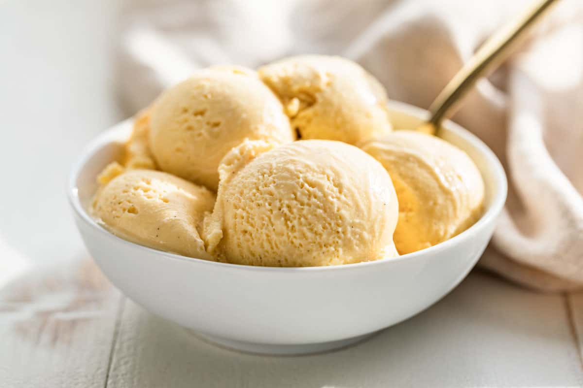 Scoops of Vanilla Ice Cream in a white bowl with a gold spoon.