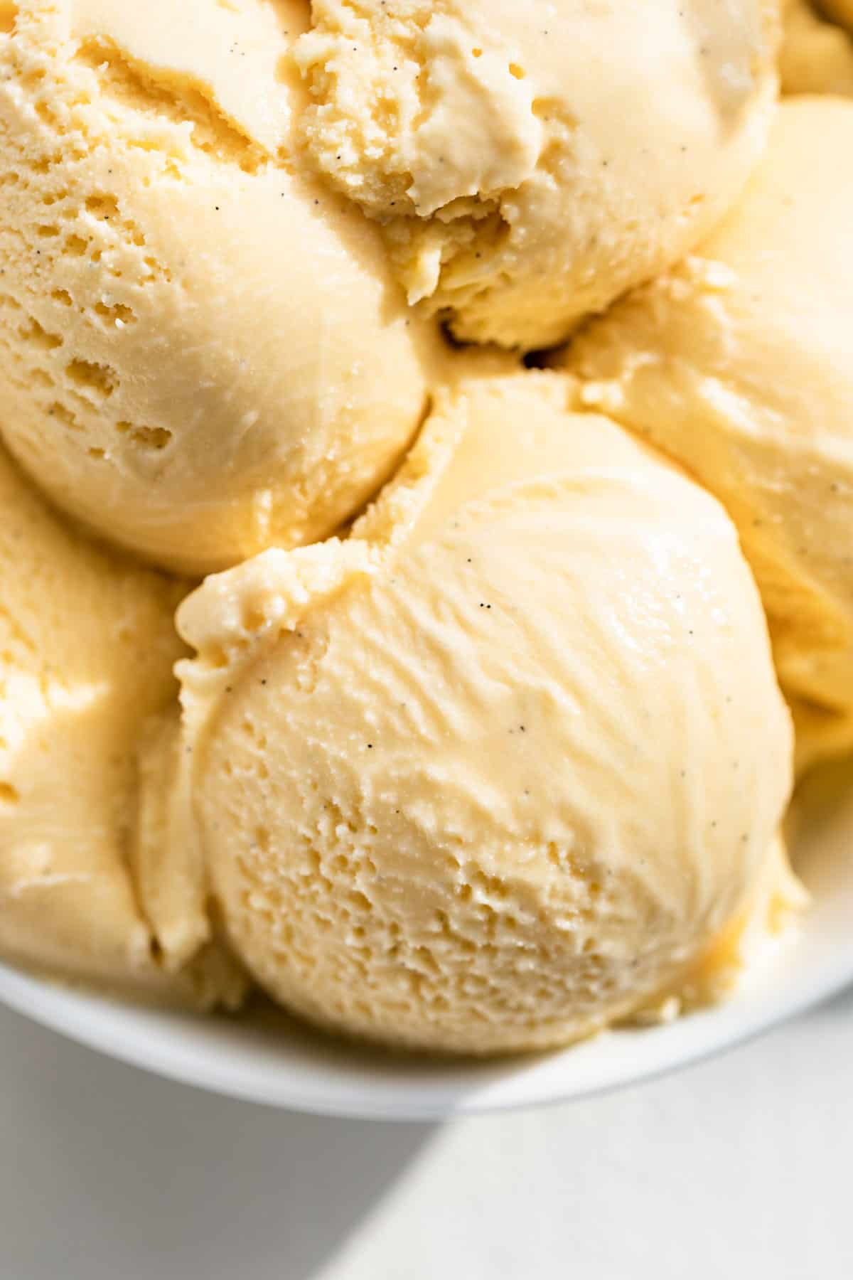Close view of scoops of vanilla ice cream in a white bowl.