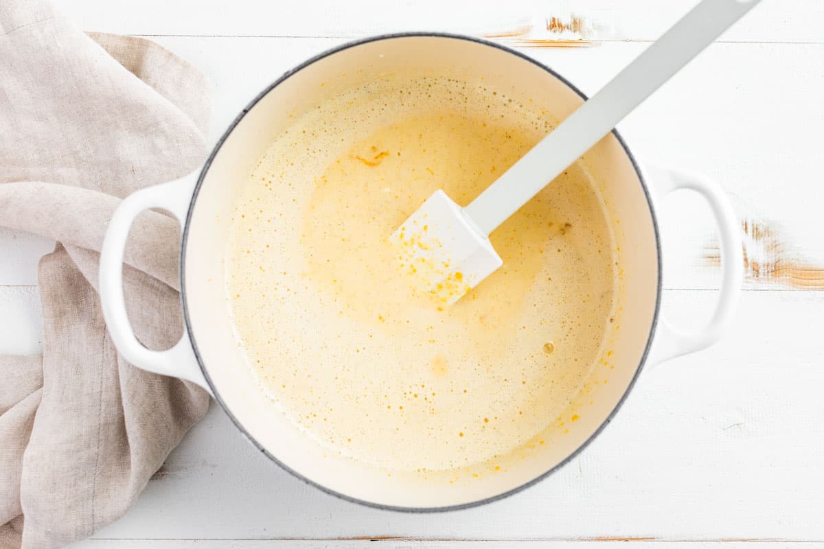 Adding the half and half to the egg yolk sugar mixture in a white cooking pot.