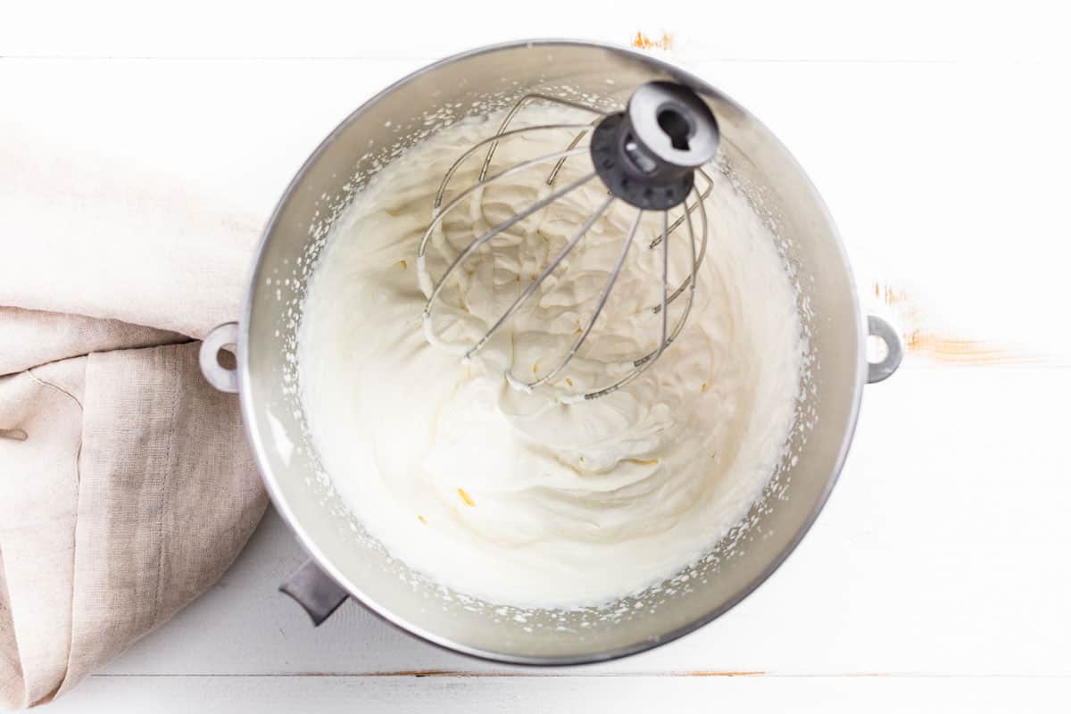 Softly whipped cream in a metal mixing bowl with the whip attachment.