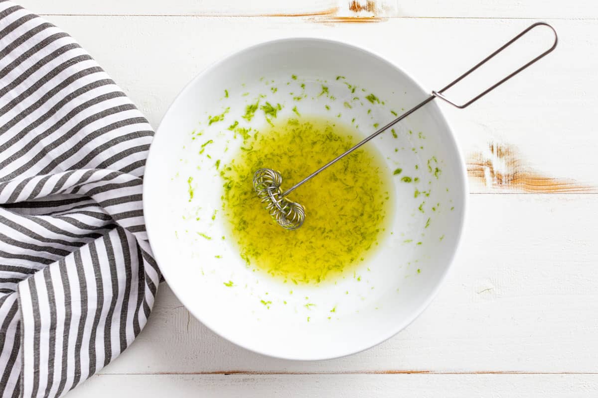 Whisking together the honey, lime zest, and lime juice in a small white bowl.