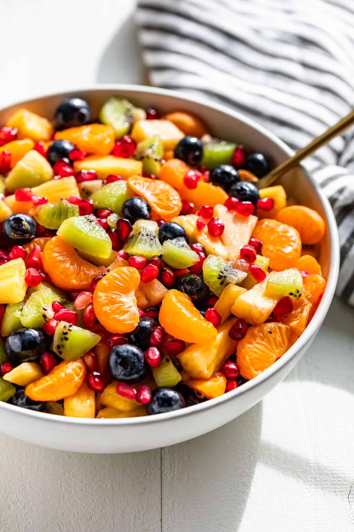 Side view of Winter Fruit Salad in a white serving bowl with a serving spoon.