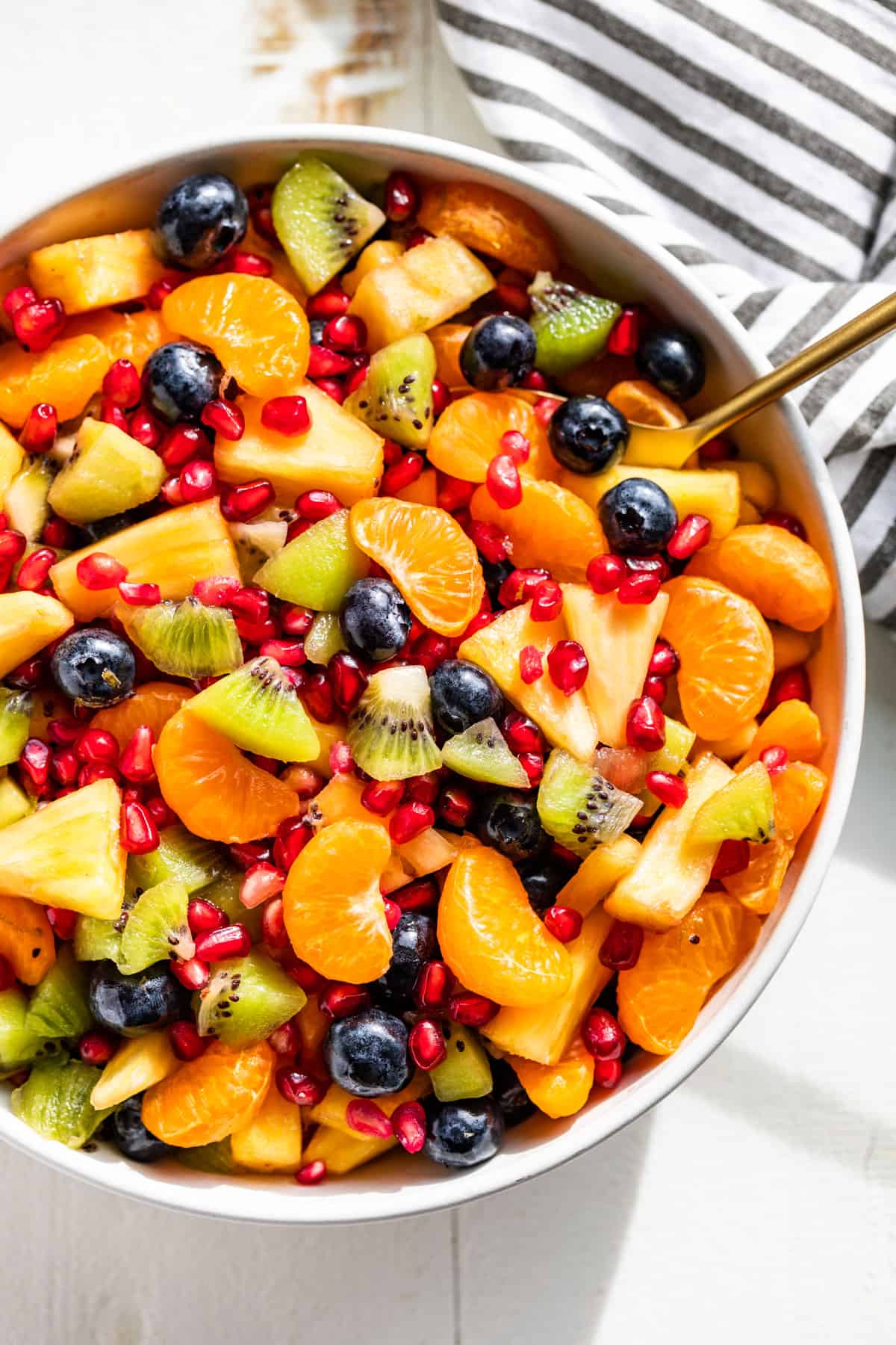 Straight down view of Winter Fruit Salad in a white serving bowl with a stripped linen on the side.