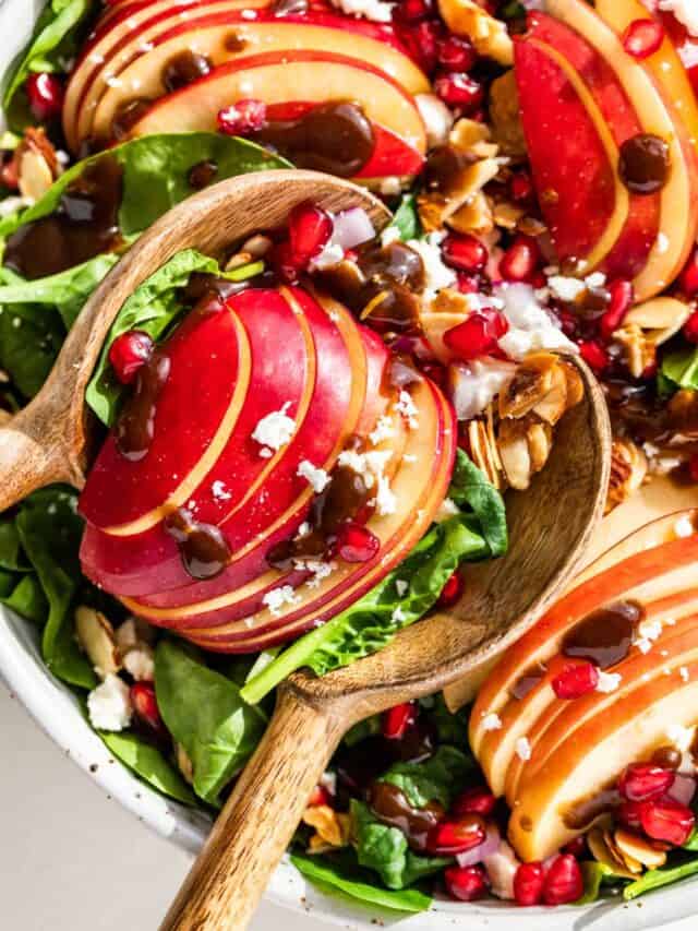 Close up view of Apple Spinach Salad with wooden spoons scooping some out.