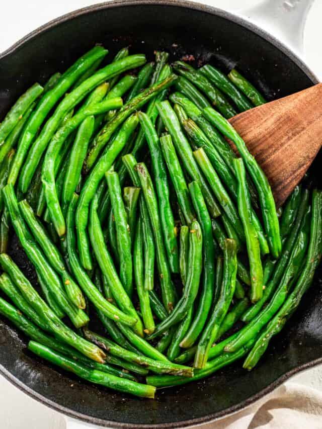 Closer downwards view of green beans in a white skillet.