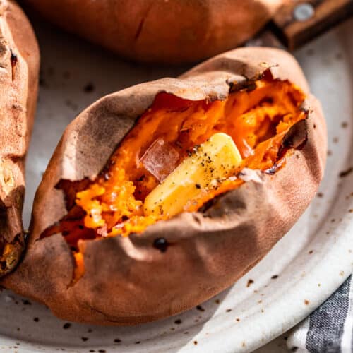 Side view of a split open Baked Sweet Potato with a pat of butter, sea salt, and pepper in the center.
