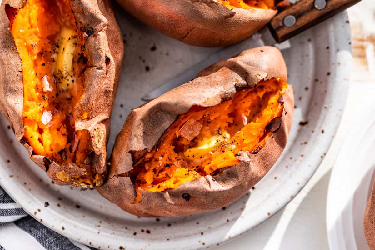 Straight down view of 3 baked sweet potatoes split open with butter, sea salt, and pepper in the centers.