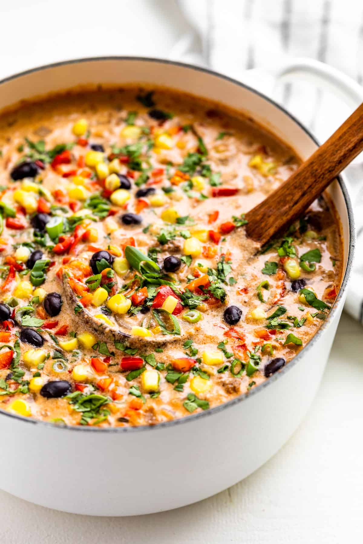 Side view of Creamy Taco Soup in a large white pot with a wood ladle in it.