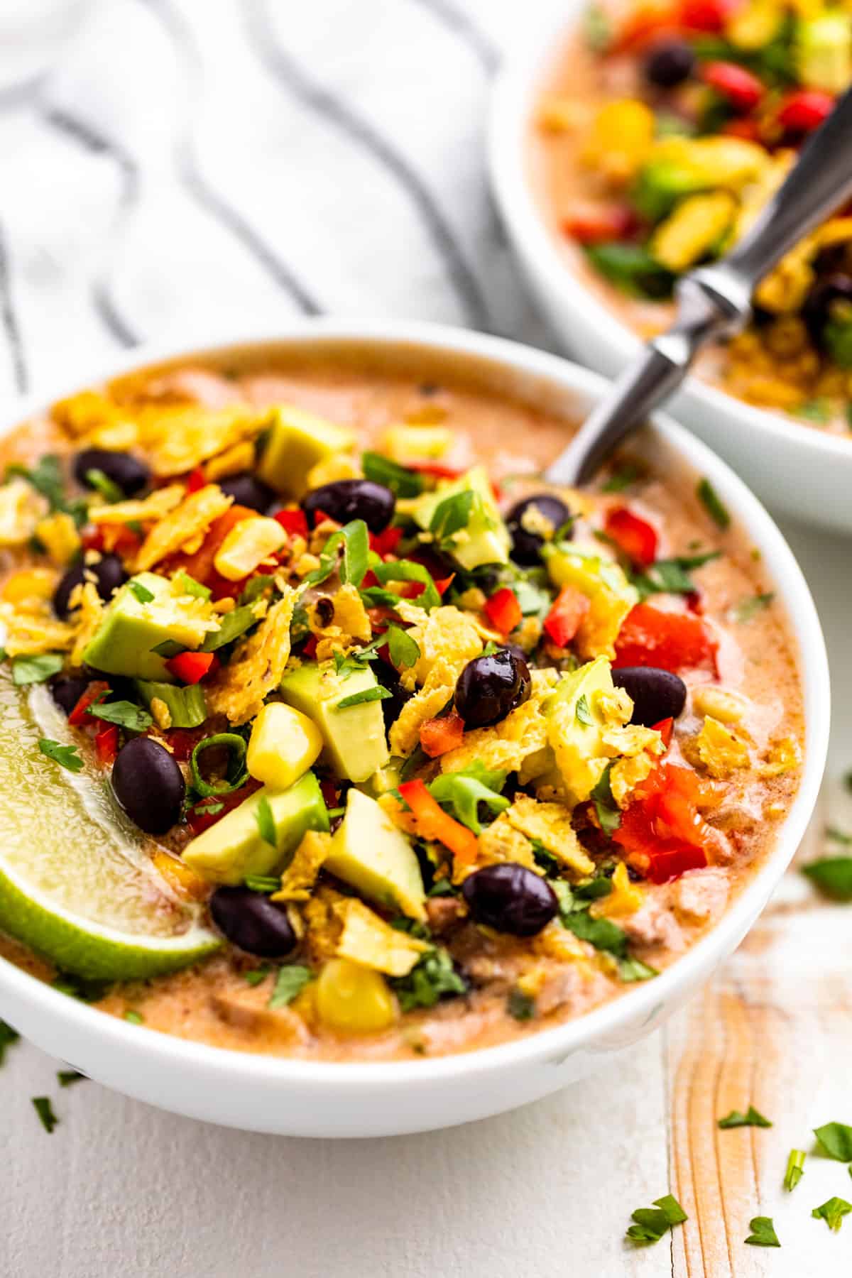 Side view of Creamy Taco Soup in two white bowls topped with black beans, corn chips, and a lime wedge.