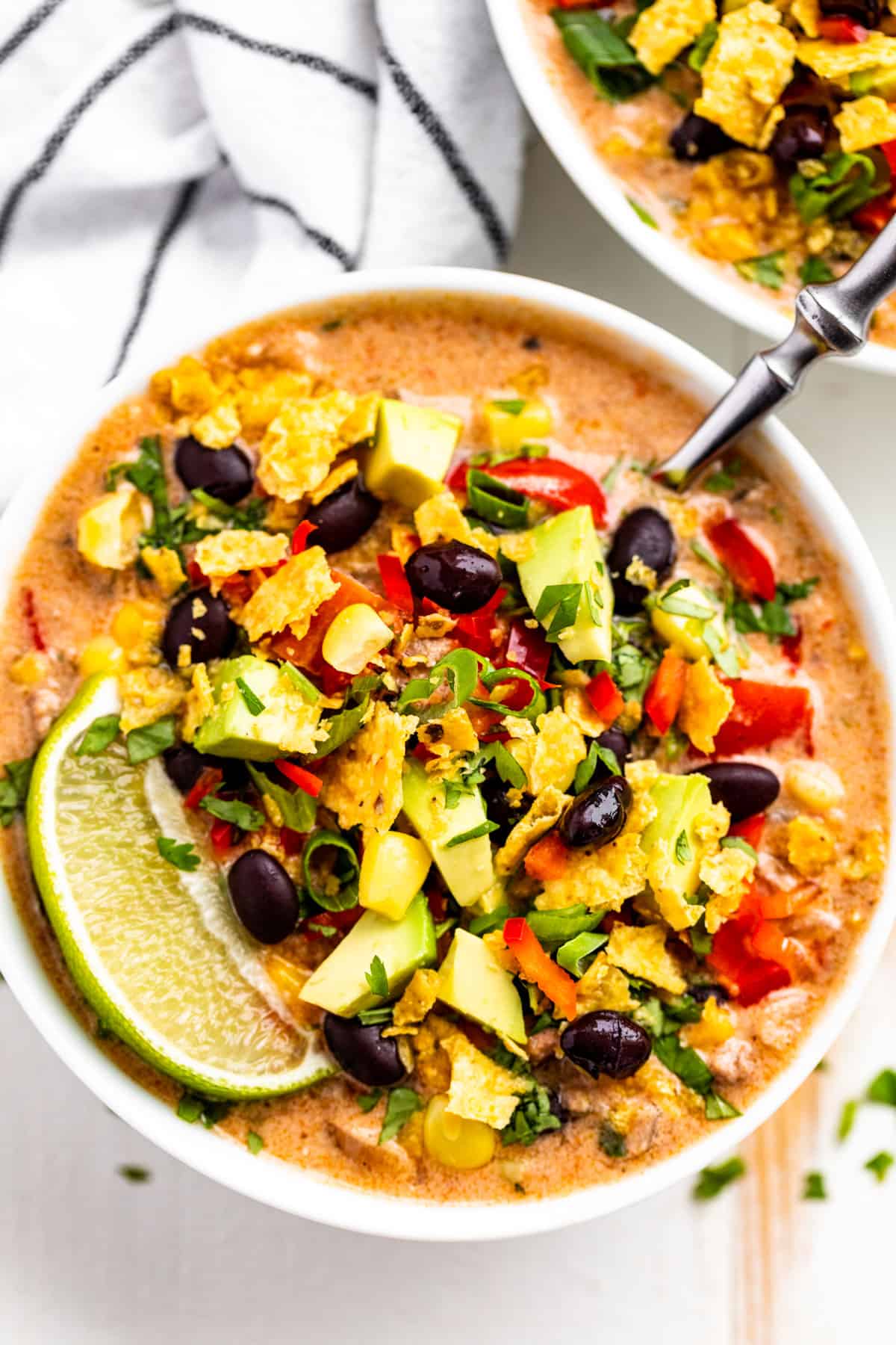 Creamy Taco Soup in two white bowls topped with corn, black beans, corn chips, and a lime wedge.