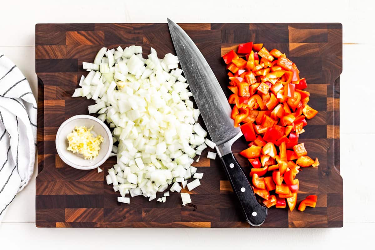 Minced garlic, diced onion and red bell pepper on a wood cutting board.