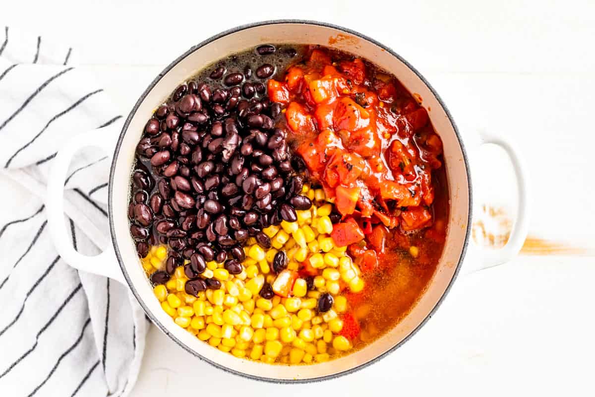 Adding black beans, corn, and fire roasted tomatoes with chilis to the soup pot.