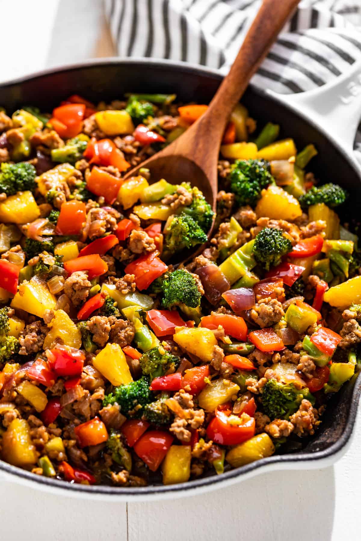 Side view of Ground Pork Stir Fry in a white skillet with a wooden spoon on the side.