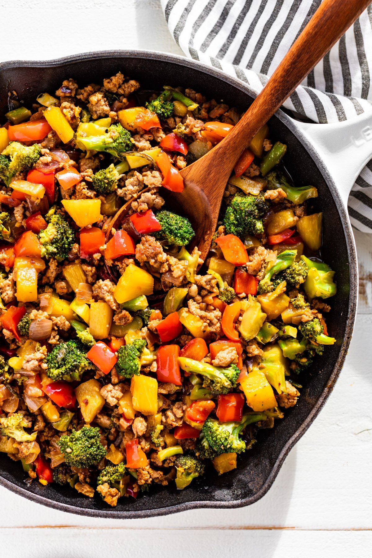 Straight down view of Ground Pork Stir Fry in a white skillet with a wood spoon scooping some out.