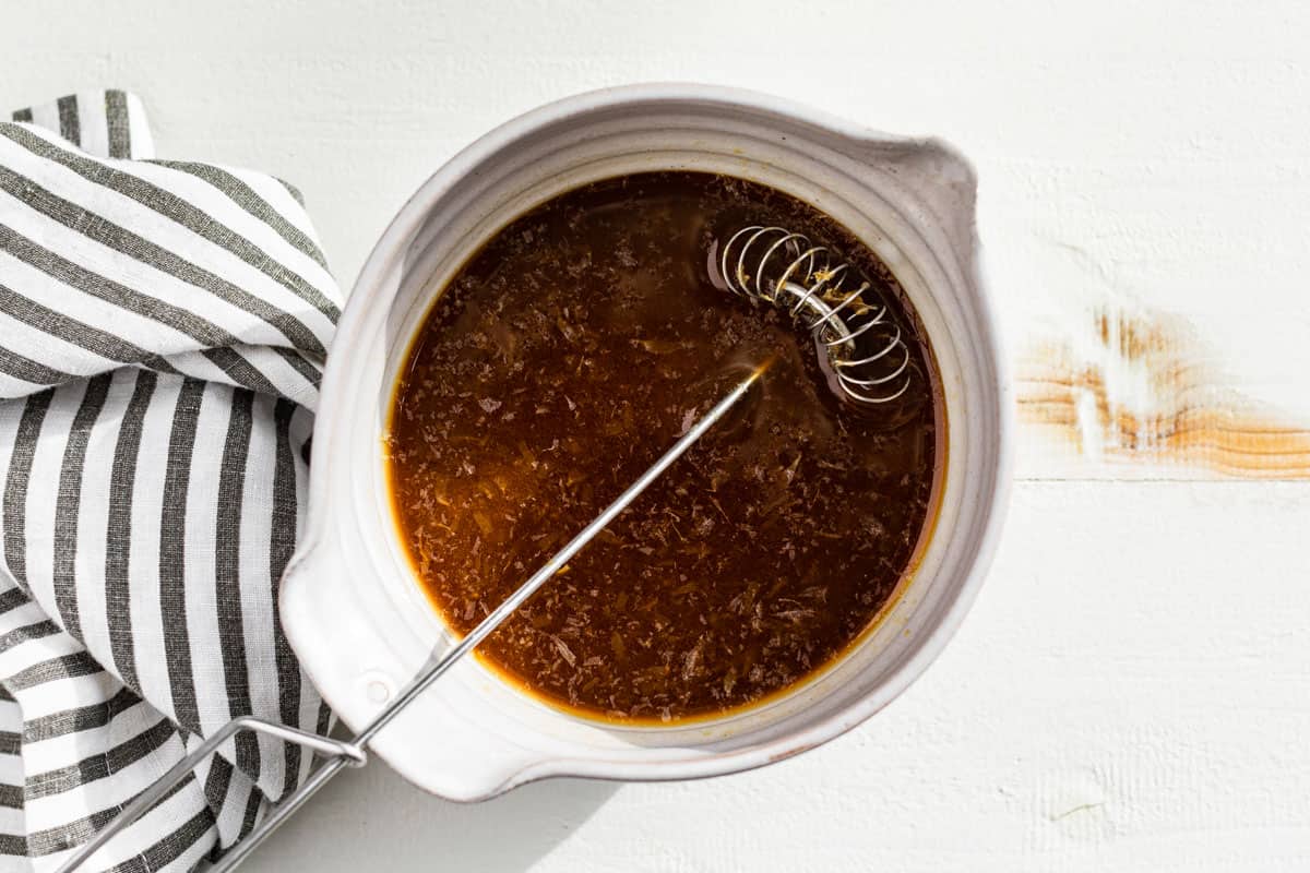 A small bowl with stir fry sauce and a whisk.