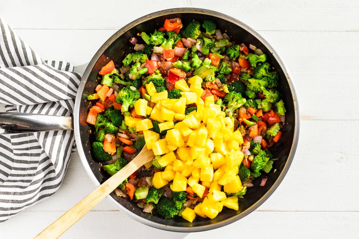 Adding the pineapple to the stir fried veggies.