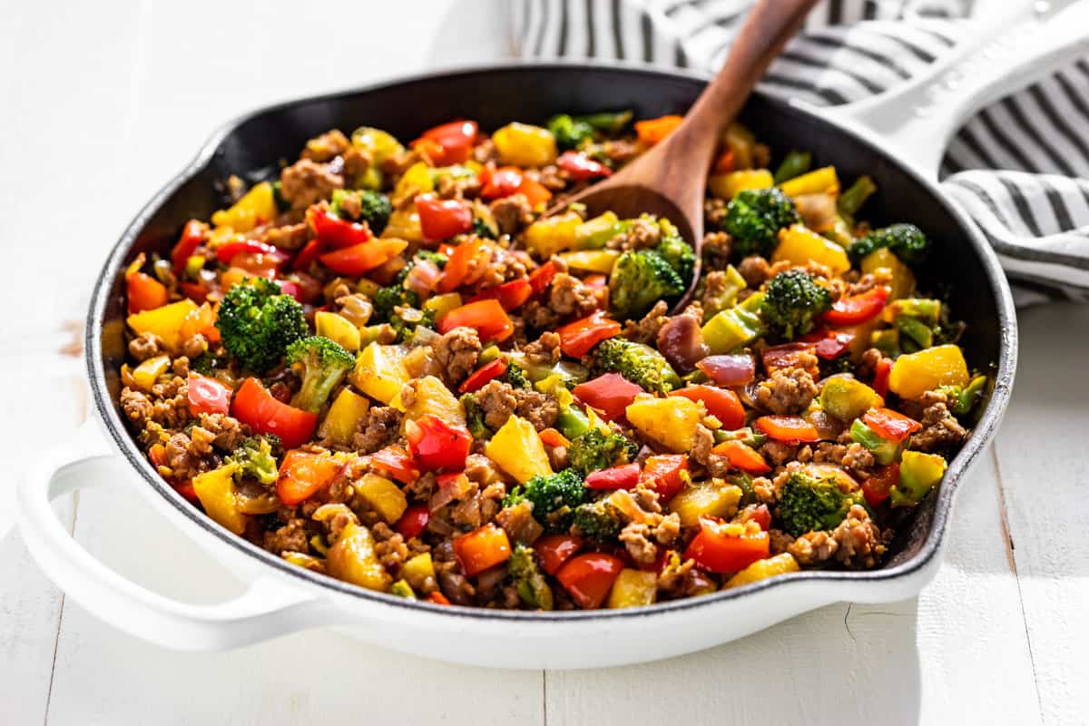 Side view of Ground Pork Stir Fry in a white skillet and a wood spoon scooping some out.