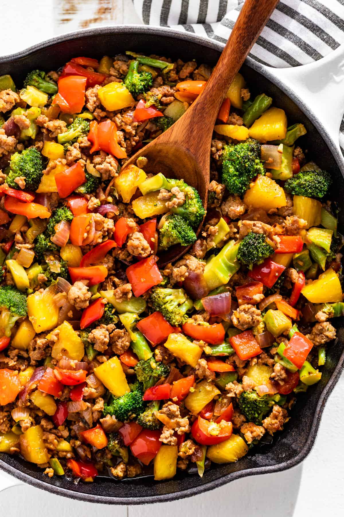 Straight down view of Ground Pork Stir Fry in a white skillet with a wooden spoon scooping some out.