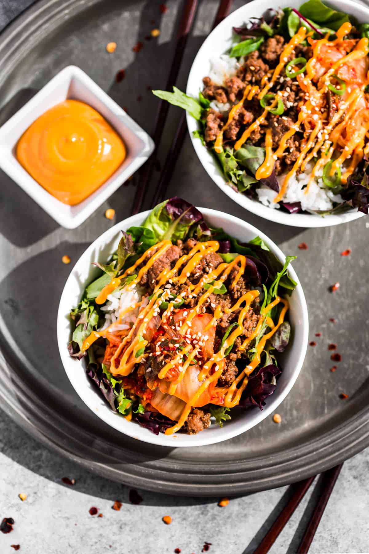 Straight down view of two Korean Ground Beef Bowls with a side of sriracha mayo and chopsticks on the side.