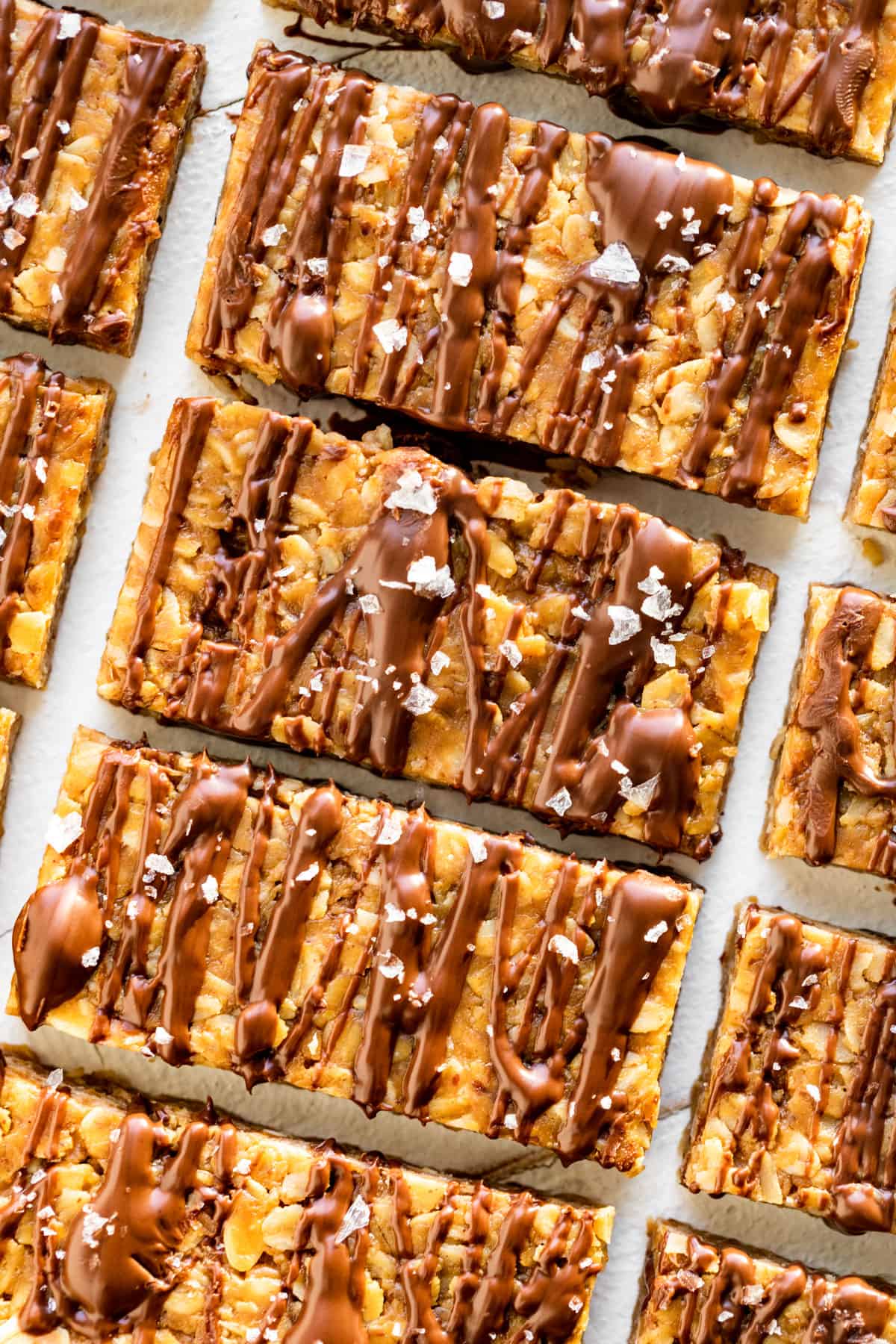 Diagonal rows of Peanut Butter Granola Bars drizzled with melted chocolate and sprinkled with sea salt.