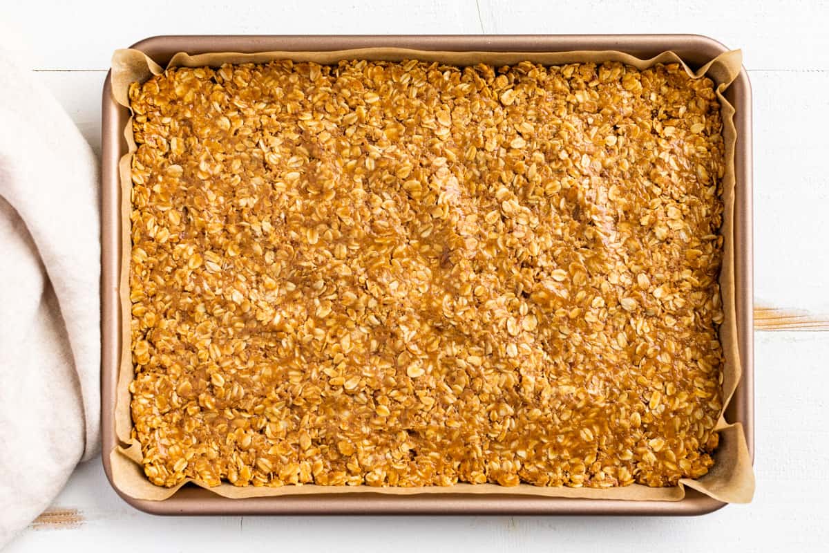 Patting out the peanut butter oat mixture into a half sized baking sheet.