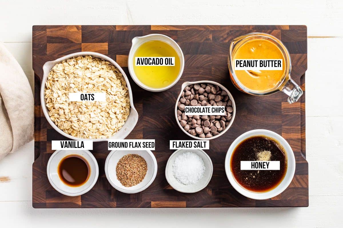 All the ingredients for Peanut Butter Granola Bars measured out in bowls, oats, peanut butter, chocolate chips, honey, vanilla, and coconut oil.