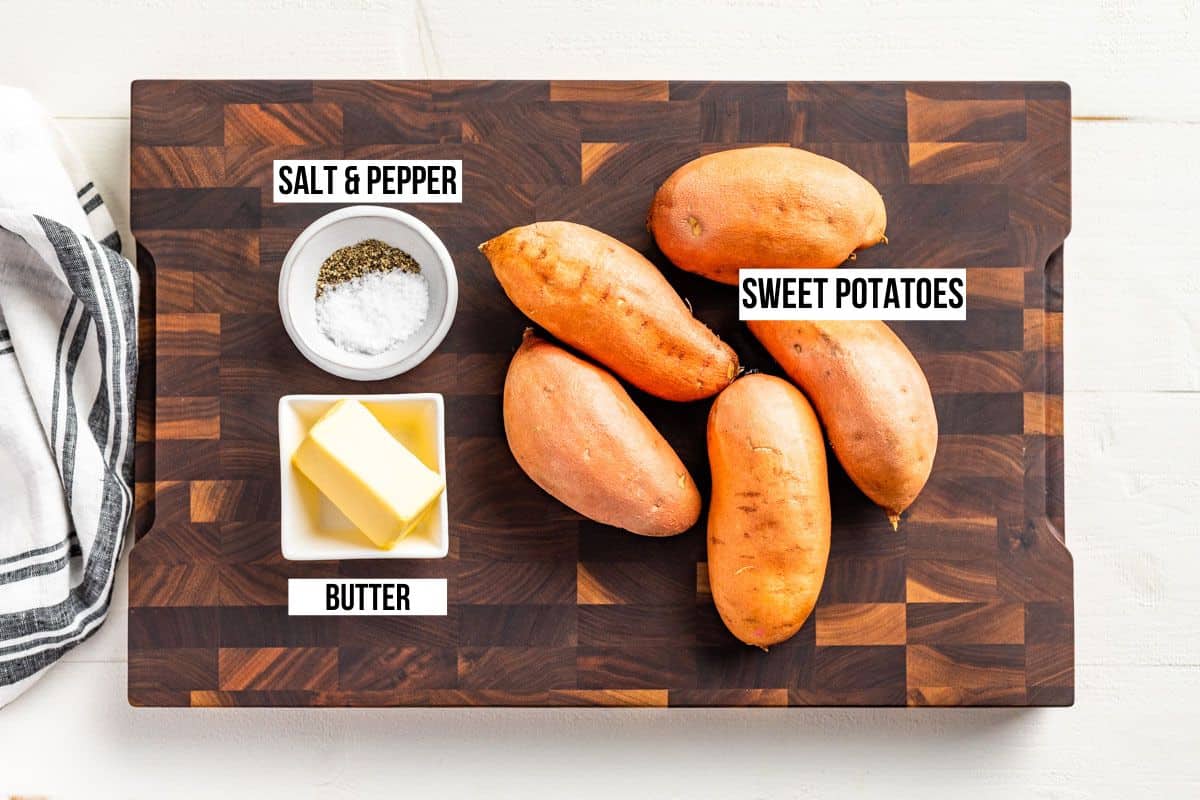 Whole sweet potatoes, butter, sea salt, and pepper on a wood cutting board.