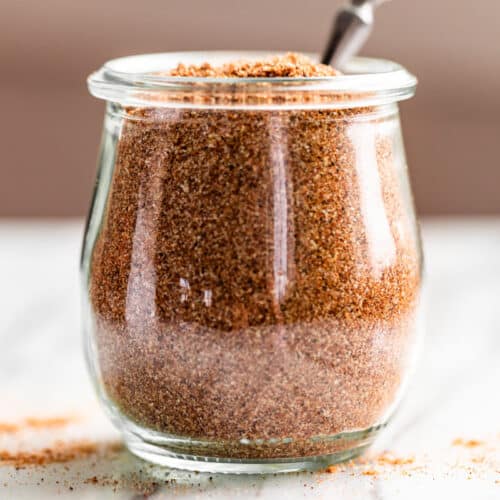 Finished Taco Seasoning in a clear glass jar with a silver spoon in it.