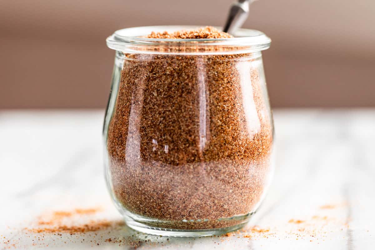 Finished Taco Seasoning in a clear glass jar with a silver spoon in it.