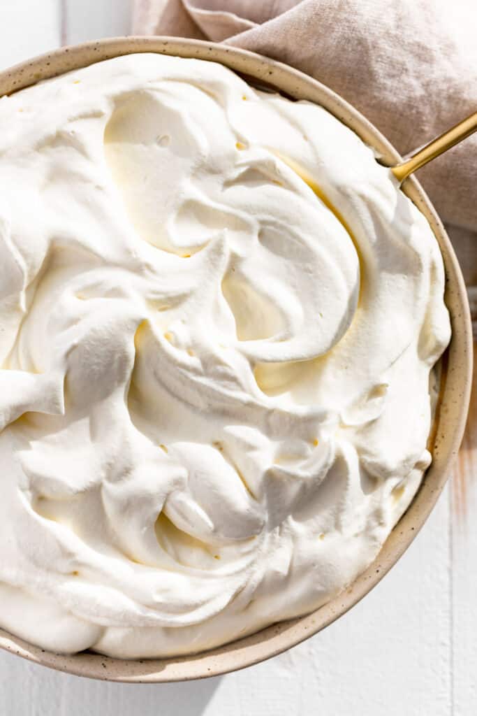 Downwards view of whipped cream in a pottery bowl with a gold spoon in it.