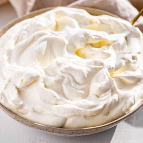 Finished whipped cream in a pottery bowl with a gold spoon in it.