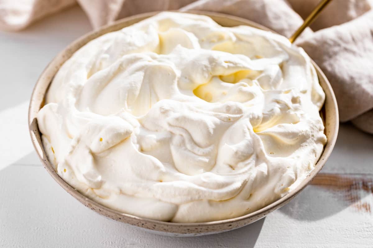 Finished whipped cream in a pottery bowl with a gold spoon in it.