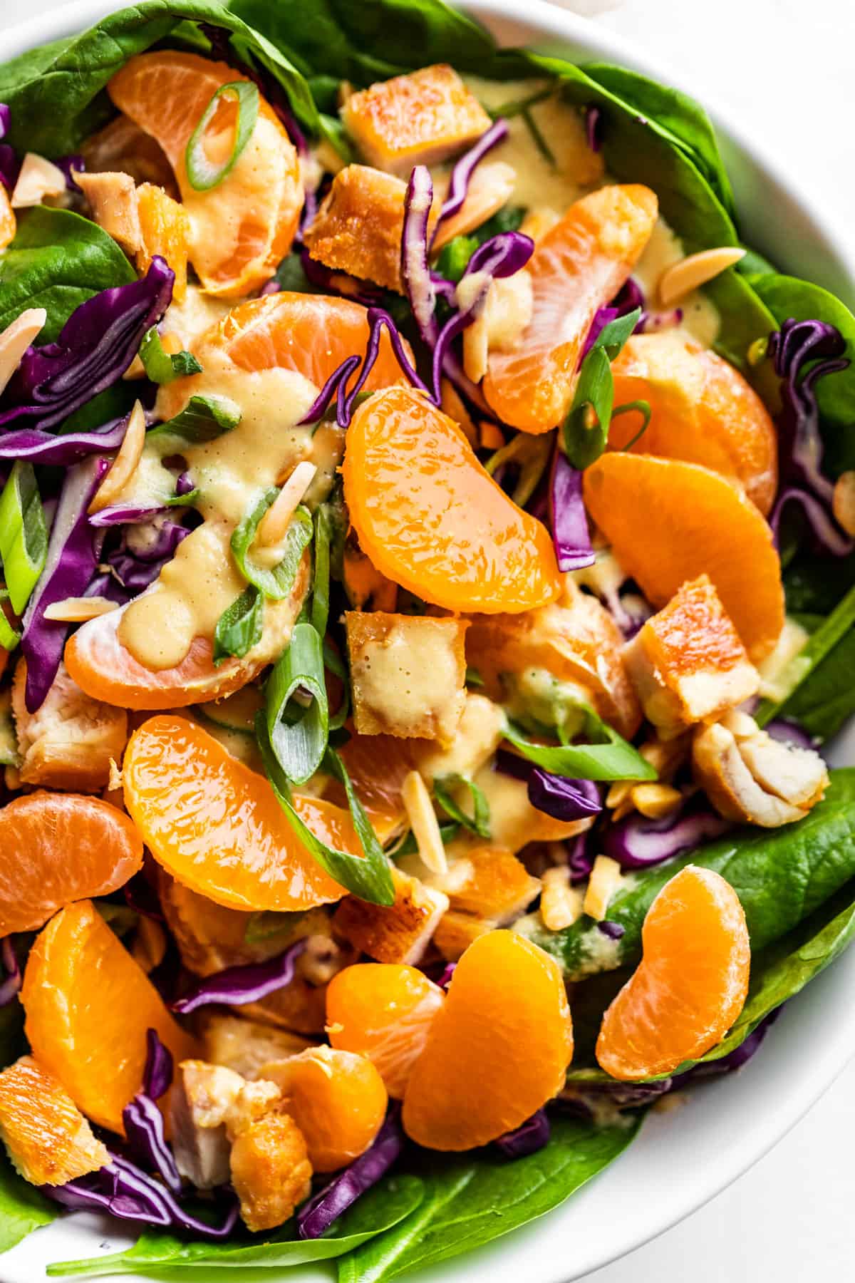 Mandarin Orange Chicken Salad in a white bowl drizzled with ginger dressing.