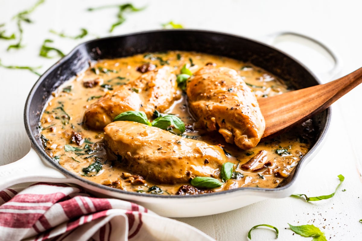 Creamy Tuscan Chicken in a white skillet with basil leave around it.